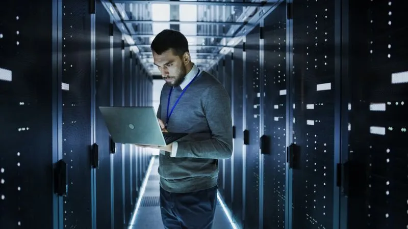 Rechenzentrum Person mit Laptop steht in einem Gang, rechts und links zahlreiche Serverschränke aufgereiht