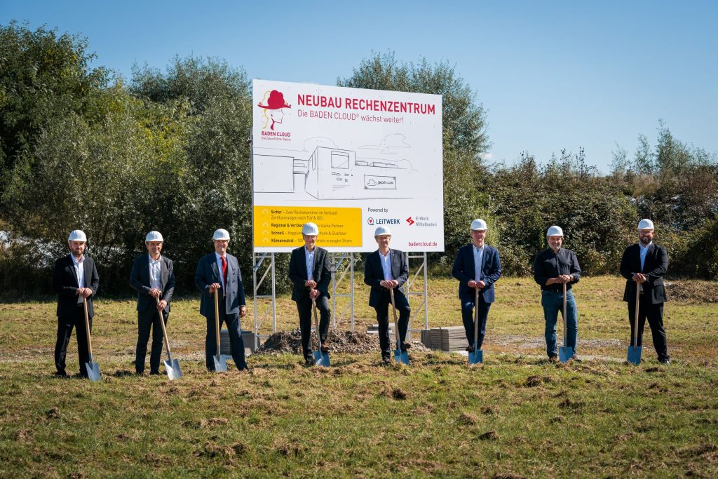 Spatenstich Neubau Rechenzentrum BADEN CLOUD® Mehrer Personen mit Spaten und Helm stehen im freien vor einem Schild mit der Aufschrift "Neubau Rechenzentrum"