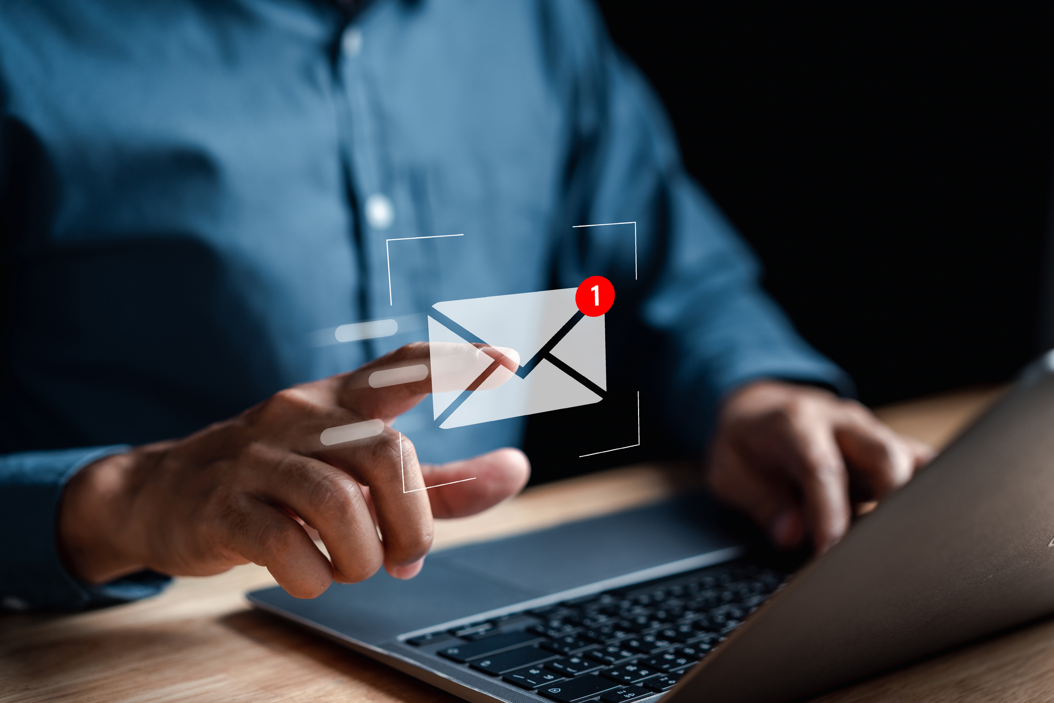 Mann vor Notebook zeigt auf virtuelles E-Mail Zeichen